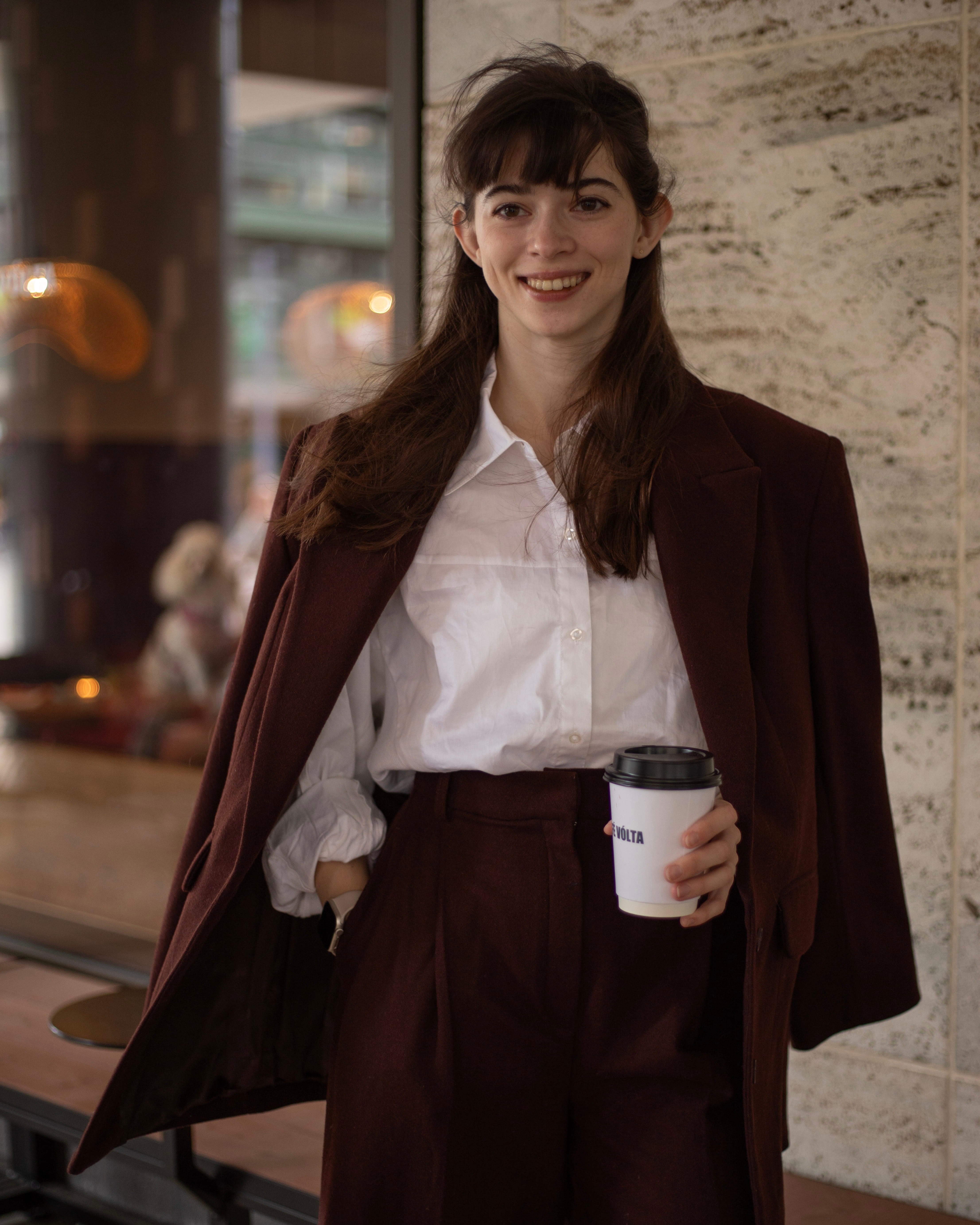 Valeriia Mykhalova standing outside a café, smiling, holding a coffee